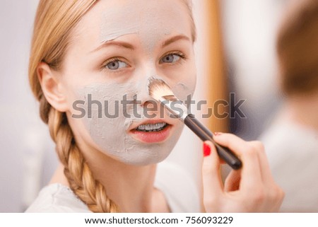 Skincare. Young woman applying with brush grey clay mud mask to her face. Female taking care of skin condition. Spa beauty treatment.