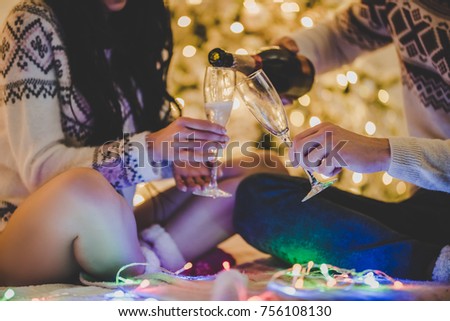 Merry Christmas and Happy New Year! Cropped image of attractive young couple is celebrating holiday at home together. Sitting on bed in sweaters and Santa Claus hats, drinking champagne and smiling.