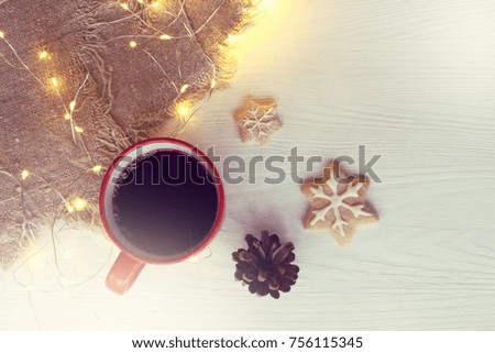 red mug with drink and figured cookie on the table with garland lights view from the top