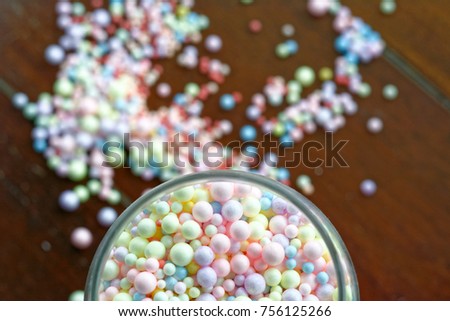many colorful of polystyrene beads in bottle and blur polystyrene beads on brown wood background