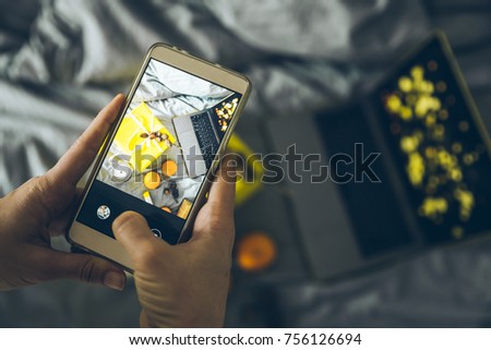 woman taking picture on her phone of present box near laptop on the bed