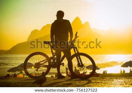 Scenic sunset view of Ipanema Beach with Two Brothers Mountain towering above the silhouette of a man with a bicycle at the Arpoador overlook in Rio de Janeiro, Brazil