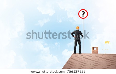 Young businessman wearing helmet with roadsign on roof edge. Mixed media