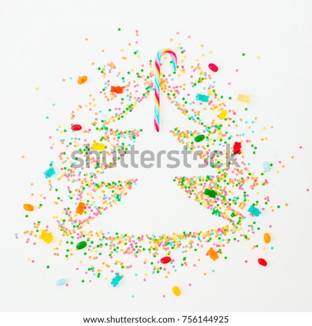 Christmas tree made of colorful bright confetti and rainbow candy cane on white background. Flat lay, top view copy space