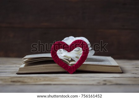 Heart handmade, open book and on top of a white rose bud on a wooden background.