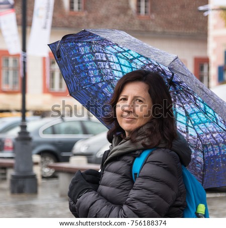A girl with an umbrella stands on a rainy day on a street in Sibiu city in Romania