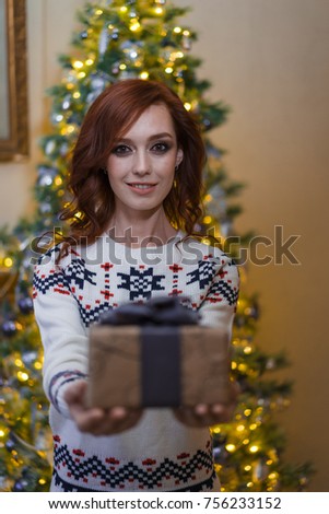 young attractive woman gives a gift on a christmas tree background
