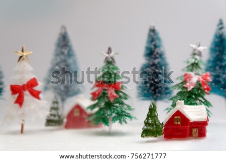 Green and white christmas tree with red ribbin behind house with snow.They are toy.