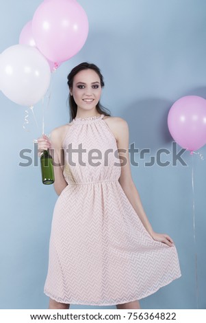 A young girl in a flower dress standing surrounded by balloons and held a green bottle
