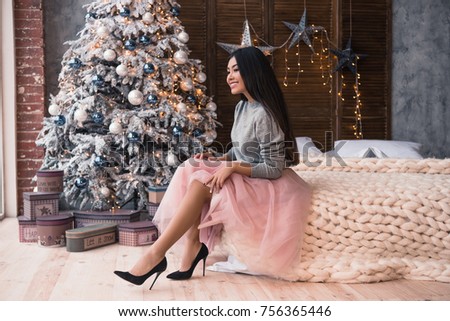 Happy New Year to you! One beautiful young asian woman is sitting on bed. She is wearing a beautiful skirt and heels