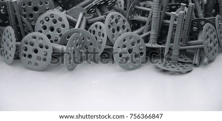 Background of many gray plastic dowels (fastening) for thermal insulation. A huge pile of plastic bolts with round holey hats lies on a gray foam polystyrene plate