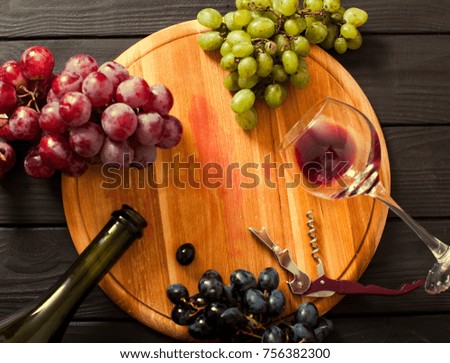White, Black and Red grapes on wooden table near bottle and wineglass on dark background