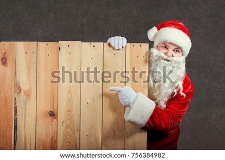 Santa Claus points to the wooden background of copyspace.