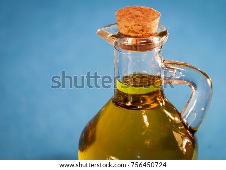 A nice looking little glass bottle with premium quality virgin olive oil closed with a cork. Oil jar close up isolated with blue background.