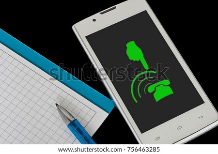 on the black surface lay a notebook with pen and white smartphone. On smartphone screen green sign of the phone and the hand that indicates the phone
