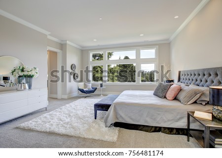 Light filled bedroom boasts a king size bed with tufted headboard dressed in grey bedding facing large white dresser topped with a round mirror. Northwest, USA