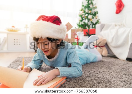 small child writes the letter to Santa lying down on the floor in the decorated living room.