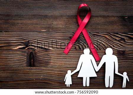 Red ribbon for HIV, AIDS, substance-abuse and anorexia awareness near paper silhouette of family on dark wooden background top view copyspace