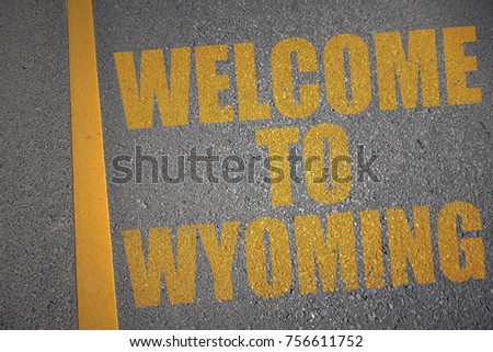 asphalt road with text welcome to wyoming near yellow line. concept