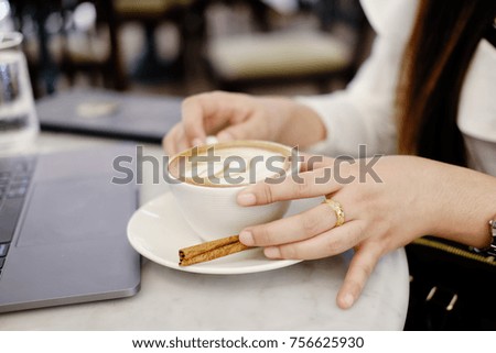 Young woman sitting in coffee shop at marble table, drinking coffee and using laptop.
