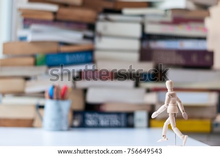 Wood manikin walking toward mountain of books blurred in the background with a blurred pencil cup. Education concept.