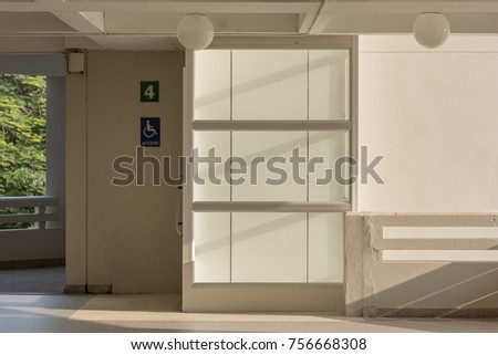 Glass elevator with disabled access sign for person who use wheelchair, convenient transport at the hotel. Universal design care for disabled person. Contrast light and shadow on wall.