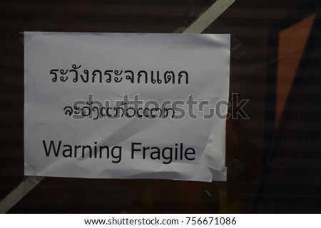 Warning message on white paper was glued on transparent glass wording is "Warning Fragile " in three languages such as Thai, Lao and English respectively