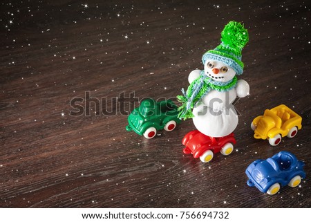 Merry christmas and happy new year greeting card with copy-space. xmas snowman standing on color toy model car. Snow background