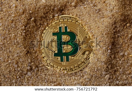 Photo of a golden bitcoin coin laying in sand.