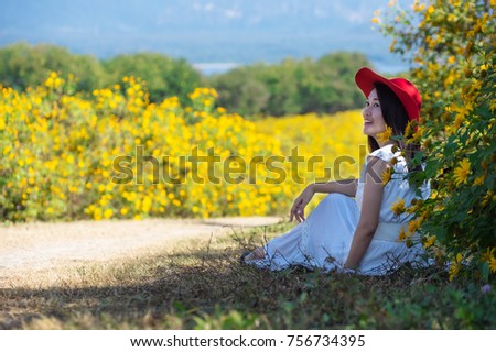 Beautiful woman in nature flower, Her wear white dresses and red hat sitting on Tung Bua Tong Mexican sunflower field in Mae Moh Coal Mine, Lampang Province, Thailand.