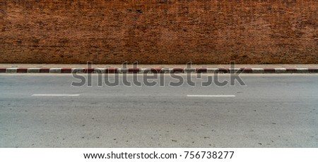 Old brown brick wall with concrete sidewalk and asphalt road with red and white traffic sign