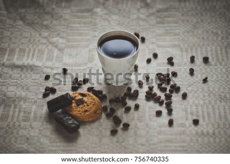 Cup of coffee with beans, chocolate, cookie on linen tablecloth.