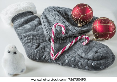 grey knitted sock and hat, red Christmas balls, sugared sticks and penguin. against white background