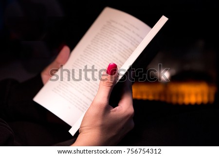 Womans Manicured Hand Holding a Book by a Fireplace