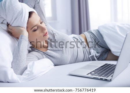 Smiling woman catching up on her social media as she relaxes in bed with a laptop computer