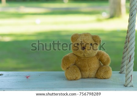 Cute Teddy bear is sitting on the wooden swing with nature background.