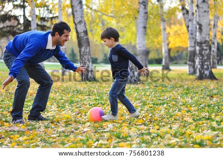 Father and son play with ball in autumn park. Happy family play soccer in public park