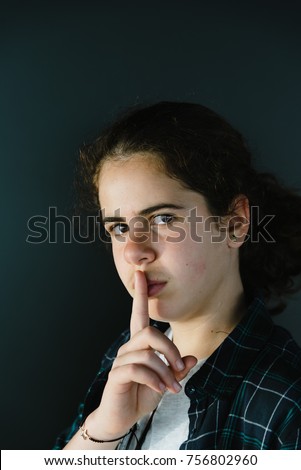 Headshot portrait of defiant teenager with finger on lips making silence gesture. Concept