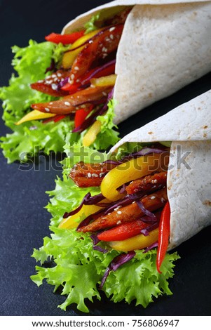 close-up of delicious fresh juicy flatbread sandwich wraps with frisee lettuce vegetables salad and  fried spicy chicken fillet on black stone tray, view from above
