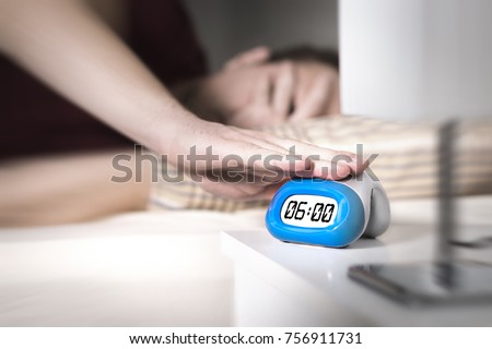Man don't want to wake up for work in the morning. Turning off alarm clock  or press snooze button with hand. Lazy person unable to get out of bed. Bad monday. Too early to get up. Royalty-Free Stock Photo #756911731