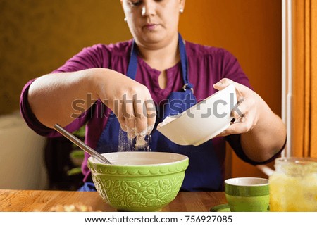 Close up photo of young beautiful adult woman with short hair, sitting behind a kitchen table, sifting the flour into the bowl, home baking concept