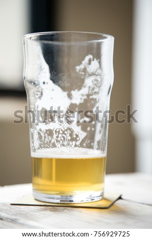 Partially drunk and almost empty beer glass with foam and dregs, on a coaster and wood picnic table at a local craft brewery