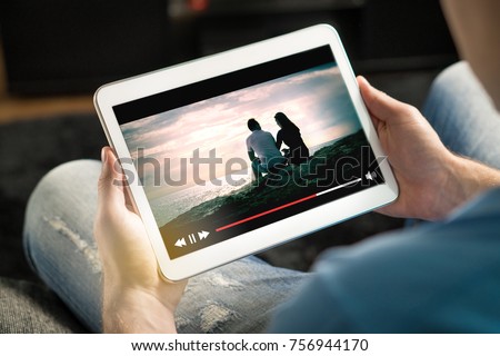 Online movie stream with mobile device. Man watching film on tablet with imaginary video player service. Royalty-Free Stock Photo #756944170