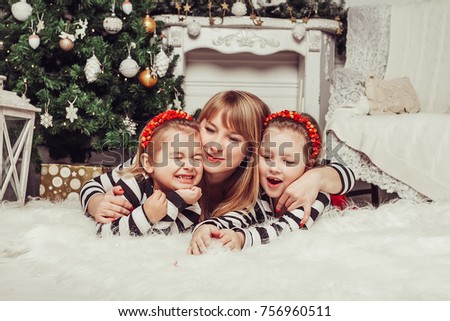 Merry Christmas and Happy Holidays! Mom and daughters near the Christmas tree indoors. The morning before Xmas. Portrait loving family close up.