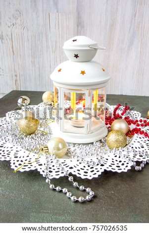 Christmas picture. White metal star light box with a burning candle, decorative elements: red and silver beads, golden toy balls at metal plate