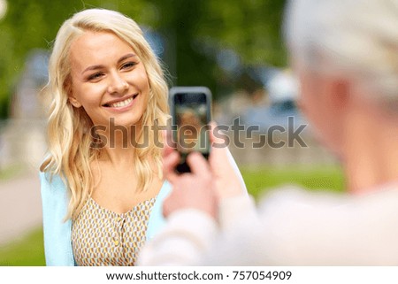 family, technology and people concept - senior mother with smartphone photographing her happy smiling young daughter at park