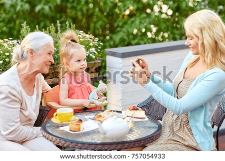 family, generation and people concept - happy smiling mother with smartphone photographing daughter and grandmother at cafe or restaurant terrace