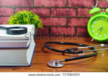 Books, desk clock, stethoscope and other thing on wooden table with brick background. Selective focused to depict educational concept, mainly on medical study or profession to be.