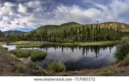 Scenic mountain landscape with morning sunlight over the mountain pass. bright summer colors reflect the sky and clouds in the river. coniferous forest on the banks of the river and on the hillside