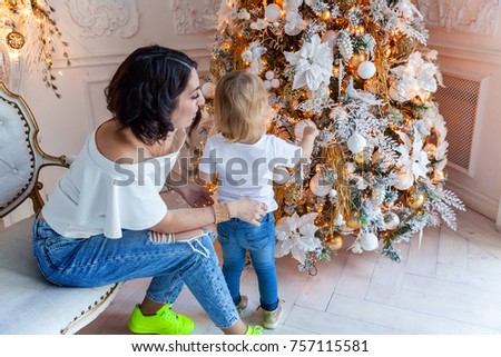 Happy family mother and daughter decorating a Christmas tree on Christmas eve at home. Woman and little girl relax in a white bedroom near the Christmas tree. Family at home.